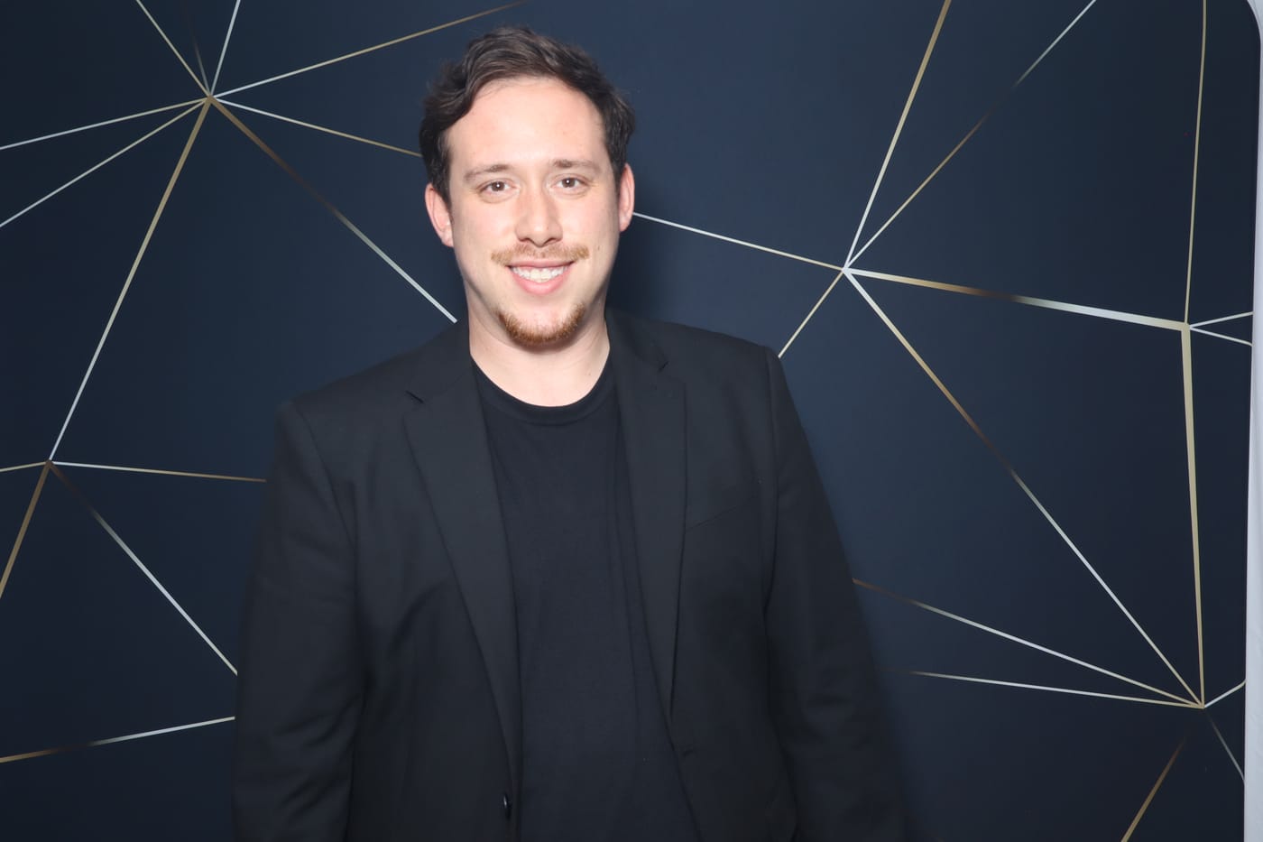 Drew Segura smiling at an event in front of a geometric backdrop