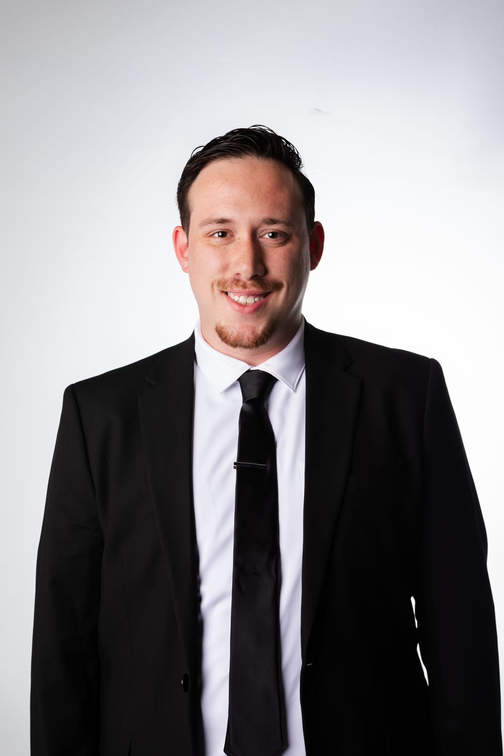 Drew Segura smiling in a black suit and tie