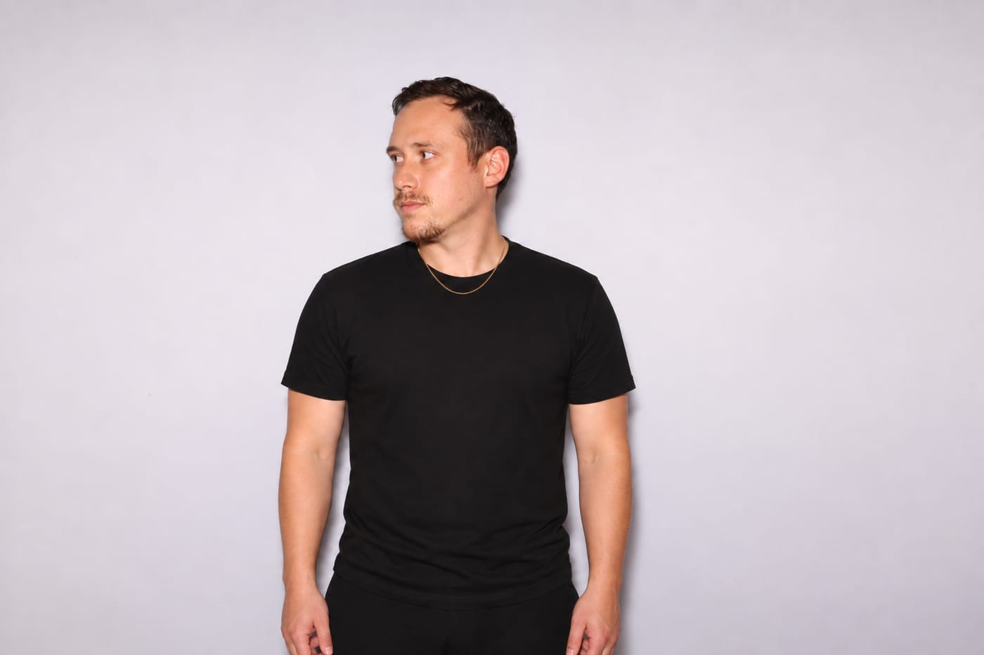 Drew in a black tee and chain, looking off camera