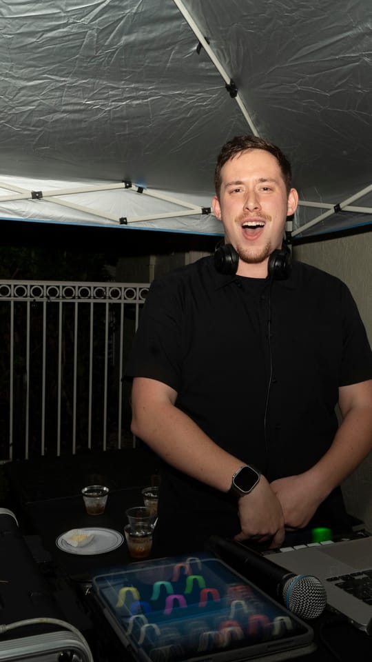 Drew laughing behind the decks at an outdoor night event