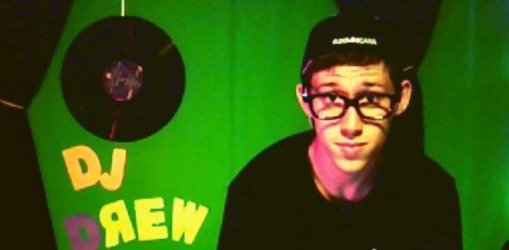 Teenage Drew in glasses and a snapback in front of his homemade DJ DREW sign